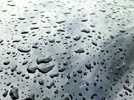 Rain drops on a black metallic car surface in a closeup view