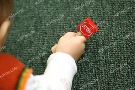 Baby haelt mini verkehrszeichen "stop" aus holz in seiner rechten hand.