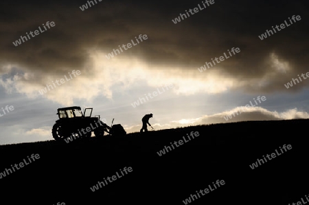Silhouette of farmer working next to his tractor up high in the clouds