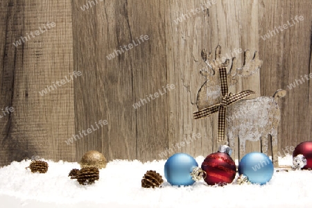 Weihnachten, Dekoration mit Holzhintergrund, Schnee, Elch, Weihnachtskugeln gold, blau und rot und Tannenzapfen
