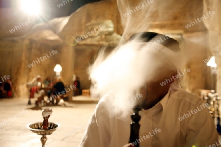 a Men smoking a Waterpipe in a cafe shop in the Village of Wadi Musa near the Temple city of Petra in Jordan in the middle east.