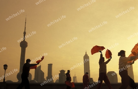 people celebrathing tai chi in the morning on the Bund in front of the skyline of Pudong in the City Shanghai in China.