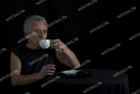 Alter Mann sitzt am Tisch Kaffe trinkend und raucht eine Zigarette