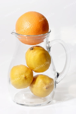 Zitronen und Orange mit  einem Glaskrug auf hellem Hintergrund