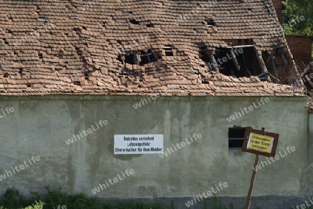 Warnschild an der Hauswand einer alten Ruine, mit teilweise eingebrochenen Dach.