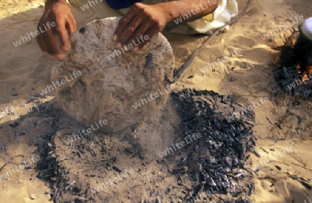 Ein Beduine beim backen von Fladenbrot an Feuerl in der Wueste bei Douz in sueden von Tunesien in Nordafrika.