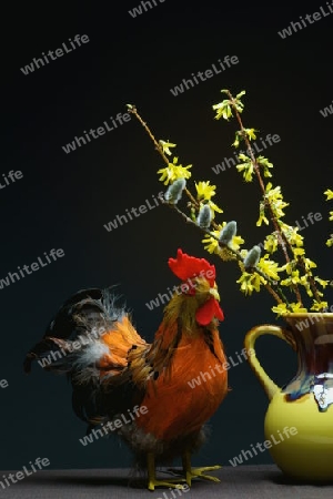 Ein Hahn als Dekoration. In der Mitte eine gelbe Vase mit einem Strauss Weide und Forsythie.