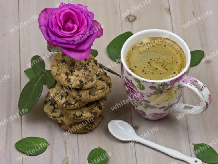 Eine Tasse Kaffee mit einem Stapel Schokoladenkekese und einer Rose.