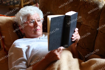 Alte Frau liegt auf Sofa und liest Buch