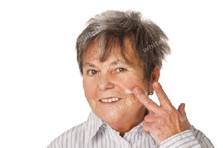 Seniorin cremt sich das Gesicht ein - freigestellt auf weissem Hintergrund