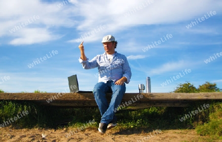 Man sitting on bench with laptop and thermos stretches to the sky - Mann auf Bank sitzend mit Notebook und Thermoskanne streckt den Mittelfinger Richtung Himmel