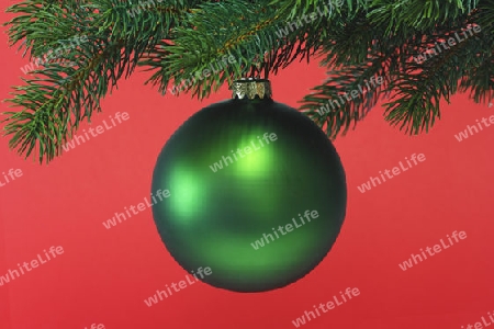 Dekorative Weihnachtskugel an einem Tannenzweig auf rotem Hintergrund