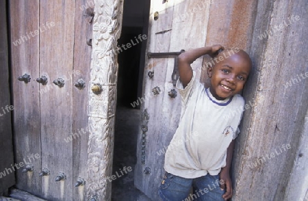Ein Junge aus Zanzibar steht an einer alten Holztuer inmitten der Altstadt Stone Town der Hauptstadt Zanzibar Town auf der Insel Zanzibar welche zu Tansania gehoert.     