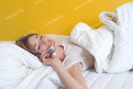 Blonde Frau telefoniert im Bett