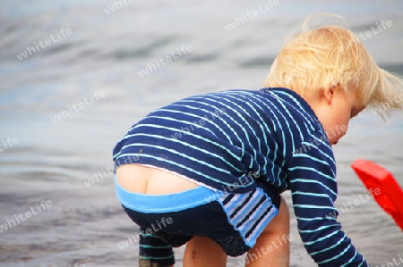 Kleiner Junger spielt mit offensichtlichem und unbek?mmerten "Maurerdekoltee" am Strand. 