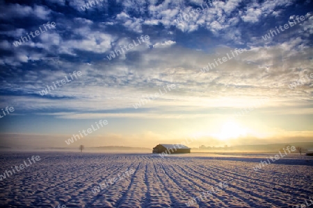 Hut at sunrise, winter with snow and light haze in conjunction with a dark blue sky, in this there are beautiful cumulus clouds.