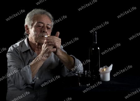 Alter Mann sitzt am Tisch und trinkt Wein und raucht eine Zigarette