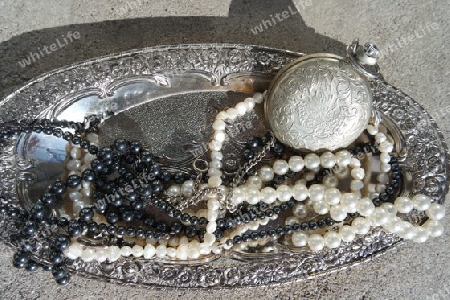 Perlenketten und Taschenuhr auf einem silbernen Tablett