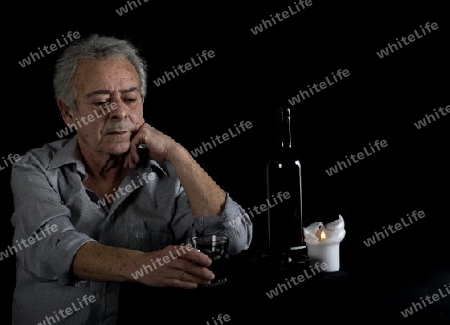 Alter Mann sitzt am Tisch und trinkt Wein