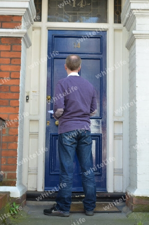 Male canvasser knocking on a blue door and standing outside