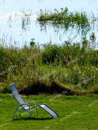 Liegewiese am See mit einsamen Liegestuhl