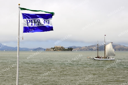Fahne von Pier 39 und historisches Segelboot in der San Francisco Bay, Im Hintergrund die Insel Alcatraz, San Francisco, Kalifornien, USA