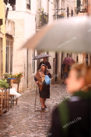 Eine alte Frau bei Regenwetter in einer Gasse in der  Altstadt von Alfama in der Innenstadt der Hauptstadt Lissabon in Portugal.    