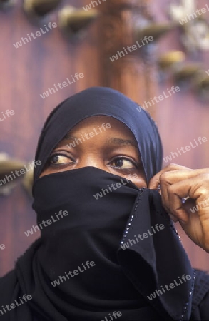 Eine Frau aus Zanzibar in traditionelle Kleidung im Portrait inmitten der Altstadt Stone Town der Hauptstadt Zanzibar Town auf der Insel Zanzibar welche zu Tansania gehoert.         