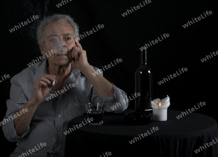 Alter Mann sitzt am Tisch und trinkt Wein und raucht eine Zigarette