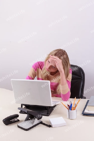 Junge Frau sitzt mit Kopfschmerzen am Computer
