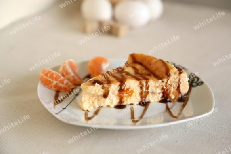 Kaesekuchen mit mandarinen und caramel-uberzug. Der teller ist mit drei mandarinenscheiben dekoriert.