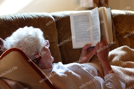 Alte Frau liegt auf Sofa und liest Buch