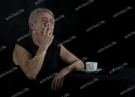 Alter Mann sitzt am Tisch und raucht eine Zigarette