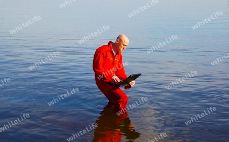 Bald man with sunglasses and red suit with notebook in the sea - Mann mit Glatze, Sonnenbrille und rotem Overall mit Notebook im blauen Wasser