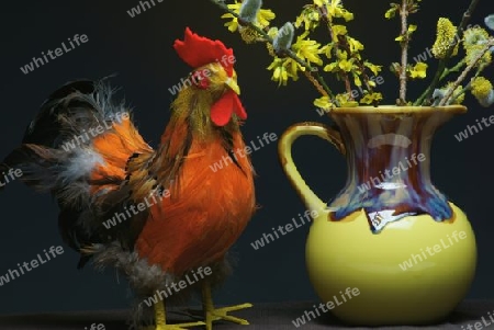 Ein Hahn als Dekoration. In der Mitte eine gelbe Vase mit einem Strauss Weide und Forsythie.